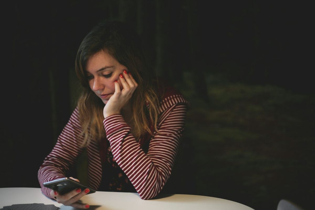 Jovem pensativa olhando o celular enquanto procura apartamento para alugar