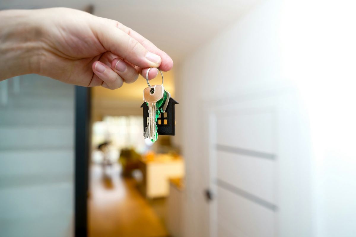 Mão segurando as chaves de um apartamento com chaveiro em forma de casinha